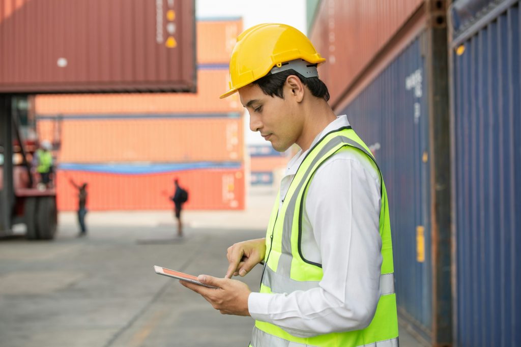 Asian male staff worker using digital tablet checking on stock shipping order at container warehouse